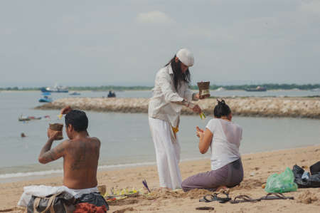 BALI, INDONESIA-APRIL, 2020: Traditional Balinese blessing ceremony by ocean, featuring newlyweds and an elder, shaman, monk or clergyman. Priest conduct the ceremony on the shore. Soft focus.のeditorial素材