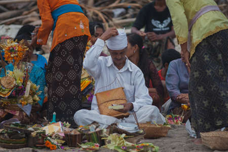 BALI, INDONESIA-APRIL, 2020: Traditional Balinese blessing ceremony by ocean elder, shaman, monk or clergyman. Priest conduct the ceremony on shore. Soft focus.のeditorial素材