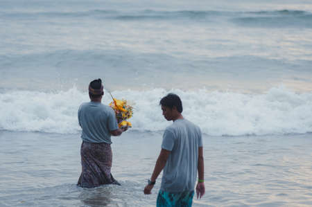 BALI, INDONESIA-APRIL, 2020: Traditional Balinese blessing ceremony by ocean elder, shaman, monk or clergyman. Priest conduct the ceremony on shore. Soft focus.のeditorial素材