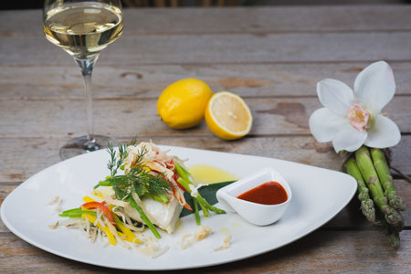 White fish seabass fillet with vegetables and white wine on a wooden table in a restaurant with decor. Tasty and healthy food. A cozy evening in a restaurant during a date. Beautiful table setting.の写真素材
