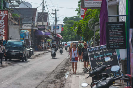 KUTA, BALI, INDONESIA-APRIL, 2020: City landscape, view of narrow streets Asian village crowded pedestrians, parked motorcycles. Bright signs of shops and restaurants on streets. Travel to tropics.のeditorial素材