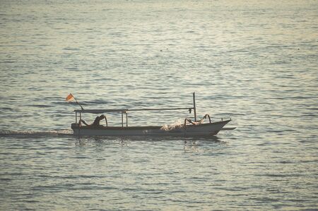 Seascape, fishing boat in the ocean during sunset. Atmospheric photo from a trip to the island of Bali. Travel to Asia. Soft focus. Traditional fishing boats.の写真素材