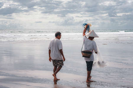 KUTA, BALI - APRIL, 2020: Balinese fisherman with a net and fish catch on the ocean. Travel to Asia. Traditional methods of catching fish by throwing a net. National character. Travel concept.