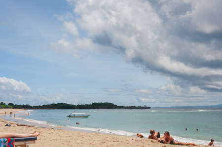 NUSA DUA, BALI, INDONESIA-SPRING, 2020: Vacationing young people are sunbathing Nusa Dua sandy beach. Travel and beach holidays on a tropical island. Families children and people.のeditorial素材