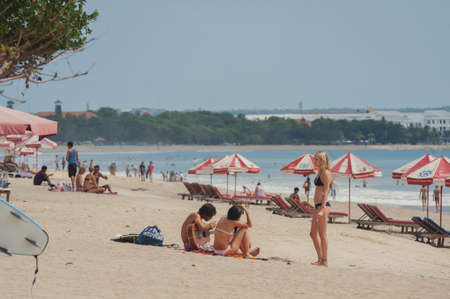 NUSA DUA, BALI, INDONESIA-SPRING, 2020: Vacationing young people are sunbathing Nusa Dua sandy beach. Travel and beach holidays on a tropical island. Families children and people.のeditorial素材