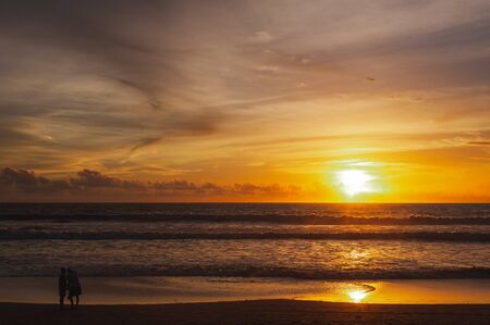 Large bright circle of the sun in the clouds touches the ocean at sunset. Touchdown. Magical dramatic sunset on a tropical beach. Seascape, ocean waves and bright clouds in the sky. Golden hour.の写真素材