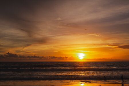 Large bright circle of the sun in the clouds touches the ocean at sunset. Touchdown. Magical dramatic sunset on a tropical beach. Seascape, ocean waves and bright clouds in the sky. Golden hour.の写真素材