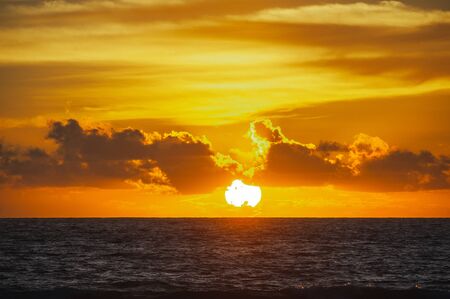 Large bright circle of the sun in the clouds touches the ocean at sunset. Touchdown. Magical dramatic sunset on a tropical beach. Seascape, ocean waves and bright clouds in the sky. Golden hour.の写真素材