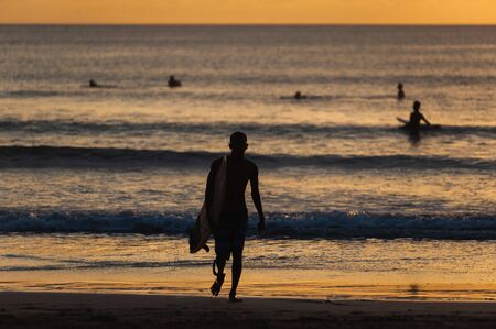 Magical dramatic sunset on tropical beach. Black silhouette of a surfer with a board on background ocean and sky during sunset. Seascape, ocean wave. Soft focus, no noise reduction.の写真素材