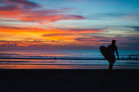 Magical dramatic sunset on tropical beach. Black silhouette of a surfer with a board on background ocean and sky during sunset. Seascape, ocean wave. Soft focus, no noise reduction.の写真素材