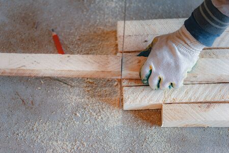 Wooden blocks on the floor during woodwork. Hands of a craftsman with a ruler and a pencil. Repair and woodwork. Soft focus, tinting and close-ups.の写真素材
