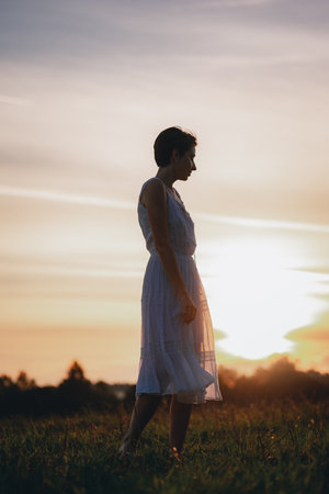 Girl in a white dress walks in the field during sunset. Walk at sunset.Natural landscape. Country life. Environment. Ecology and farming. Soft focus and toning.の写真素材