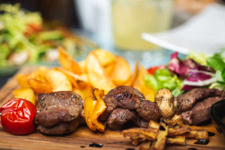 Meat, shish kebab, grilled, barbecue with baked potatoes and vegetables on a wooden plate on the tableの写真素材