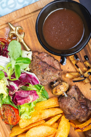 Meat, shish kebab, grilled, barbecue with baked potatoes and vegetables on a wooden plate on the...