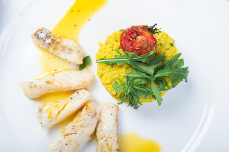 Fillet of white fish in sauce on a plate with garnish and herbs. Full lunch, main courses on a white plate. Close-up, soft focus and beautiful bokeh. Fillet of cod, sea bass, fish on a plate.の写真素材