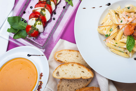 Top view of a restaurant table served with a Lentil soup, Italian penne pasta with salmon and caprese salad. Complex lunch. Complete and varied food.の写真素材