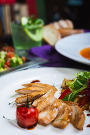 Baked chicken breast with vegetables and sun-dried tomatoes on a plate, lunch served for guests on a table in a restaurant. Full lunch. Tasty food. Soft focus and beautiful bokeh.の写真素材