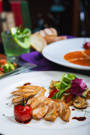 Baked chicken breast with vegetables and sun-dried tomatoes on a plate, lunch served for guests on a table in a restaurant. Full lunch. Tasty food. Soft focus and beautiful bokeh.の写真素材