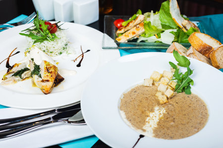 Multi-course set lunch. Mushroom soup, white fish fillet with herbs and rice, salad with chicken breast and vegetables. Complete and healthy food. Lunch is served on table in restaurant. Soft focus.の写真素材
