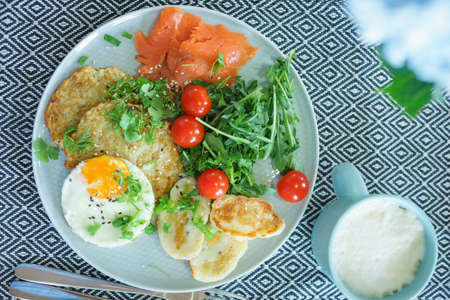 Cozy homemade breakfast: potato pancakes with scrambled eggs, red fish, cheese and vegetables with herbsの写真素材
