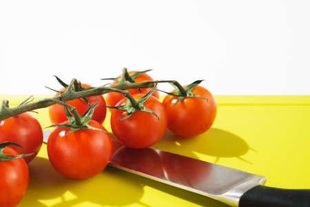 Bright red cherry tomatoes on white clean plastic cutting board with a kitchen knifeの写真素材