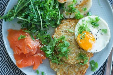Cozy homemade breakfast: potato pancakes with scrambled eggs, red fish, cheese and vegetables with herbsの写真素材