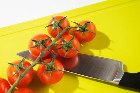 Bright red cherry tomatoes on white clean plastic cutting board with a kitchen knifeの写真素材