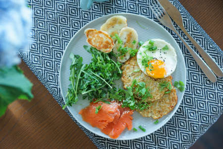 Cozy homemade breakfast: potato pancakes with scrambled eggs, red fish, cheese and vegetables with herbsの写真素材