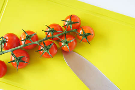 Bright red cherry tomatoes on white clean plastic cutting board with a kitchen knifeの写真素材
