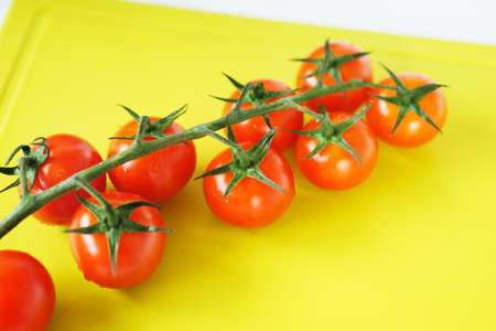 Bright red cherry tomatoes on white clean plastic cutting board with a kitchen knifeの写真素材