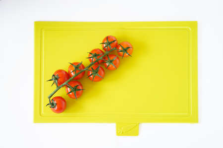 Bright red cherry tomatoes on white clean plastic cutting board with a kitchen knifeの写真素材