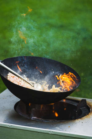 Chef prepares Chinese wok noodles over an open fire on a green lawn.の写真素材