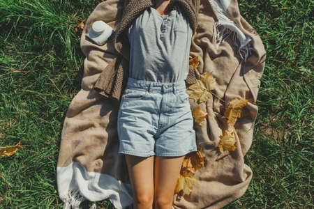 Beautiful girl in short denim shorts lies on a plaid resting on the lawn on a warm autumn day.の写真素材