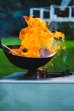 Chef prepares Chinese wok noodles over an open fire on a green lawn.の写真素材