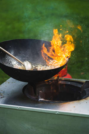 Chef prepares Chinese wok noodles over an open fire on a green lawn.の写真素材