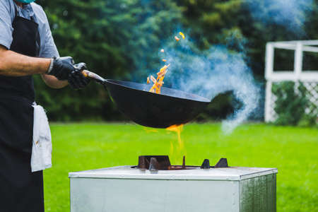Chef prepares Chinese wok noodles over an open fire on a green lawn.の写真素材