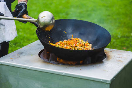 Chef prepares Chinese wok noodles over an open fire on a green lawn.の写真素材