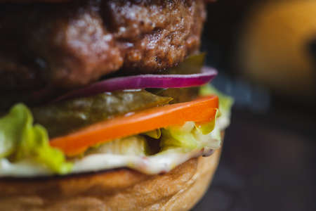 Close-up of Delicious burger with organic cutlet, cheese, vegetables and fried potatoes on a stone cutting board on wooden table with decor. Fast food in a cafe and restaurant. Menu and content, food.の写真素材