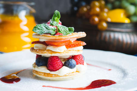 Traditional sweet pastry with three layers of airy dough with whipped cream, with strawberries and berries on a white plate on the table in a cozy cafe with decor. Close-up, macro shot.の写真素材
