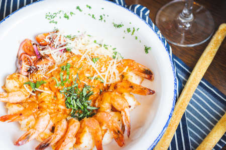Traditional bright shrimp risotto in a bowl on a table in a restaurant with a beautiful decor in a dark key close-up. Soft focus, beautiful bokeh and stylish toning.の写真素材