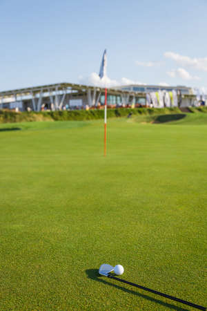 Golf ball and putter on the green grass next to the hole. Sports equipment on the grass top view. Summer vacation and hobbies.の写真素材