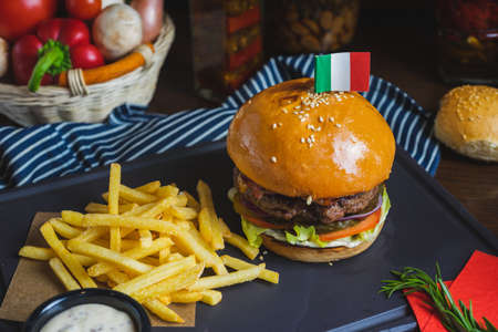 Delicious burger with organic cutlet, cheese, vegetables and fried potatoes on a stone cutting board on wooden table with decor. Fast food in a cafe and restaurant. Menu and content, food.の写真素材