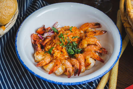 Traditional bright shrimp risotto in a bowl on a table in a restaurant with a beautiful decor in a dark key close-up. Soft focus, beautiful bokeh and stylish toning.の写真素材