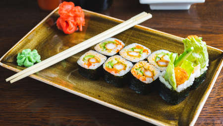 Traditional Japanese rolls with shrimps and vegetables on a plate with wooden chopsticks, close-up and soft focus. Image photos for the menu of a Japanese restaurant, content for social networks.の写真素材