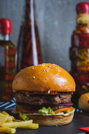 Delicious burger with organic cutlet, cheese, vegetables and fried potatoes on a stone cutting board on wooden table with decor. Fast food in a cafe and restaurant. Menu and content, food.の写真素材
