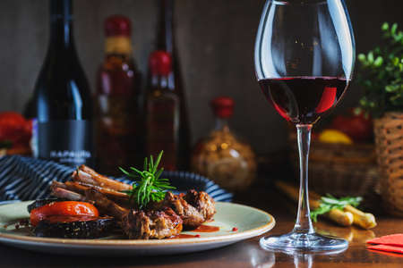 Fried ribs with a glass of red wine on a table in a restaurant close-up, in a dark key. Content for the promotion of the cafe. Soft focus and stylish toning.の写真素材