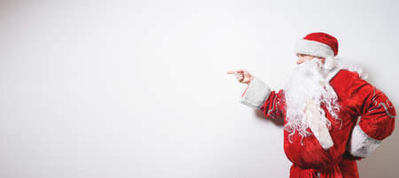 Santa Claus, old man with a white beard in a traditional red costume on a white background makes a hand pointing gesture. Christmas Holidays. Man dressed as Santa Claus isolate on white. Concept.の写真素材