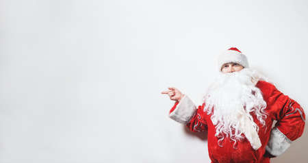 Santa Claus, old man with a white beard in a traditional red costume on a white background makes a hand pointing gesture. Christmas Holidays. Man dressed as Santa Claus isolate on white. Concept.の写真素材