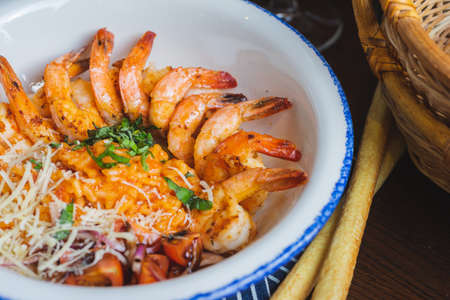 Traditional bright shrimp risotto in a bowl on a table in a restaurant with a beautiful decor in a dark key close-up. Soft focus, beautiful bokeh and stylish toning.の写真素材