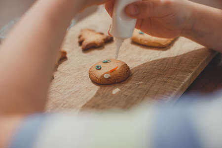 Child decorates traditional homemade Christmas gingerbread cookie for the celebration. Cozy home New Year atmosphere. Cookies for the New Year. Soft focus and stylish toning.の写真素材
